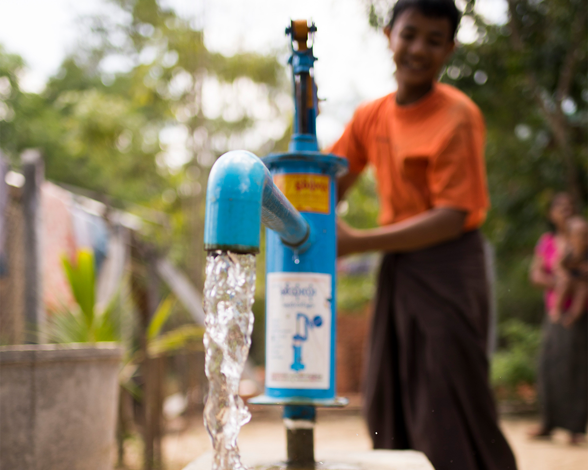 Young boy smiling from ear to ear with his eyes closes as water from a clean well pours over his hands and arms