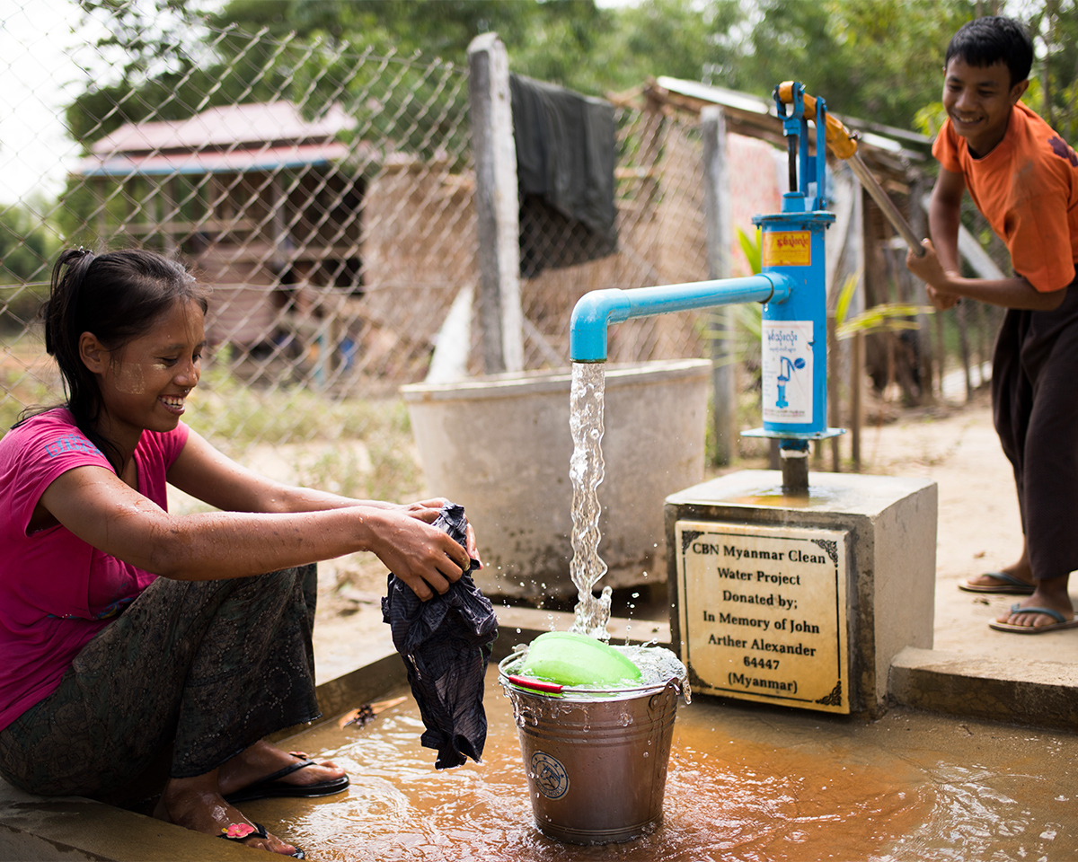 Older man on a sunny day smiling with glee as he cups his hands to drink water from a clean well