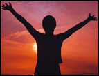 person silhouette with hands in air and sunrise in background