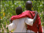 two African boys from the back walking toward a field with arms around each other