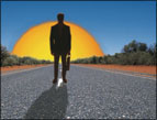 silhouette of man carrying briefcase walking on a paved road with sun rising and shadow on the road