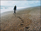person walking on beach beside ocean waves making footprints in the sand
