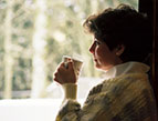 woman looking out window in winter with mug of coffee