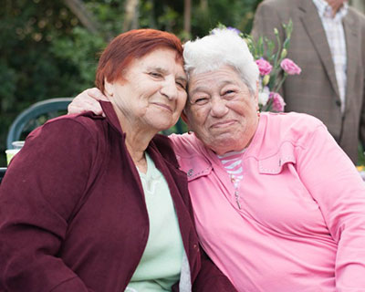 Two Holocaust survivors embracing with a smile while sitting.